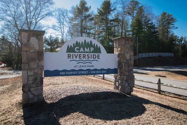 Camp Riverside sign at Lewis Park: White arch with logo over blue text on pillars.