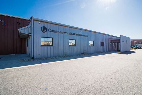 Exterior of Commonwealth Alternative Care, a building with a gray facade, blue sky, and paved parking lot.