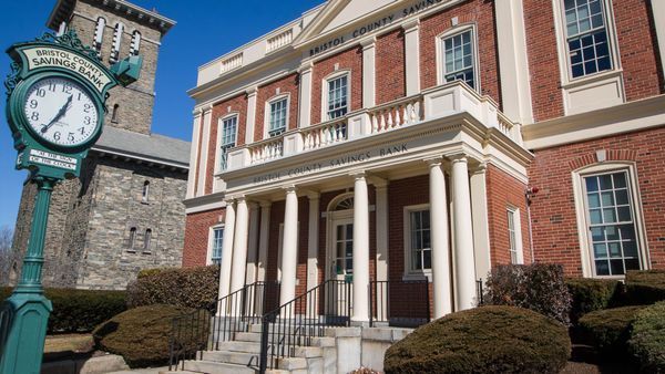 Brick building with white columns, clock tower in background.