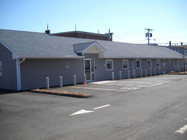Gray building with a dark roof, windows, and a small parking lot with white parking lines.