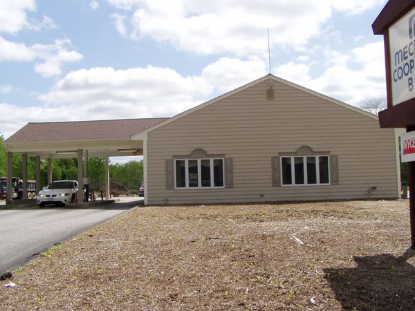 Beige bank building with drive-through, windows, and a sign under a cloudy sky.