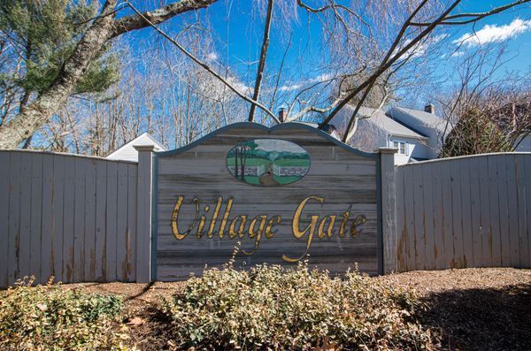Sign for Willow Gate, a wooden structure with painted scene, brown script, in front of a fence.