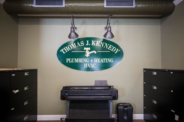 Thomas J. Kennedy Plumbing sign on green wall, with printer and filing cabinets.