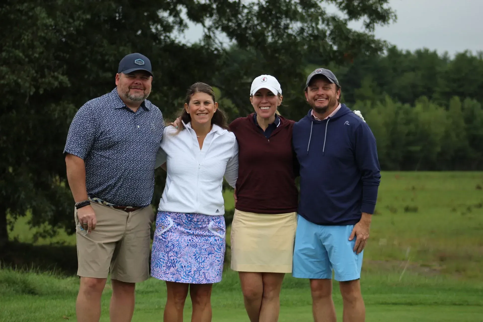Four people smiling and posing on a golf course. Two women and two men stand in front of a green field.
