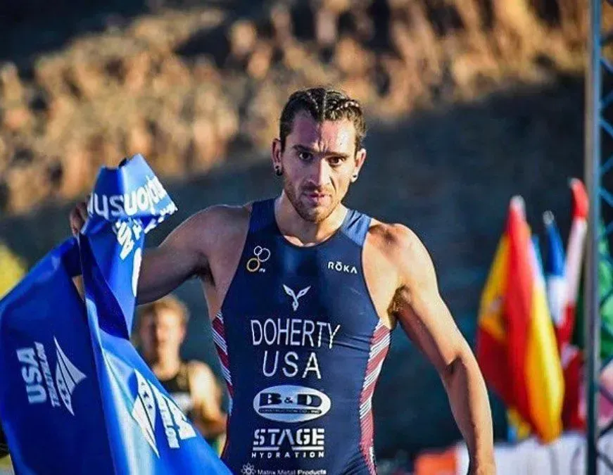 Triathlete Doherty, USA, holding blue towel, wearing a suit. Outdoor, looking at camera.
