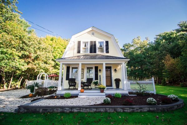 Yellow house with Dutch gable roof, white porch, black shutters, and garden.
