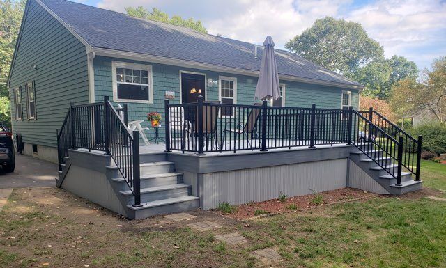 A teal house with a gray deck and black railings, steps lead to the yard on both sides.