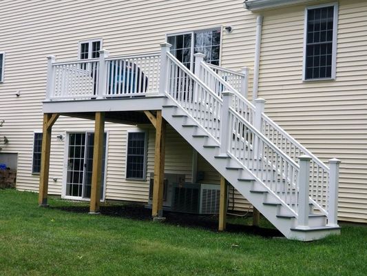 White deck with stairs against a light yellow house; a grassy lawn is in the foreground.
