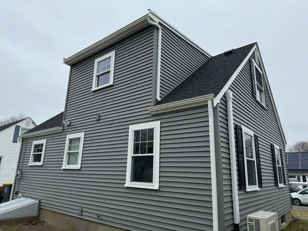 Gray-sided two-story house with white trim, windows, and black shutters under a cloudy sky.