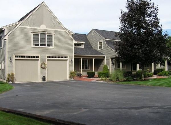 Two-story house with two-car garage, gray siding, beige garage doors, black asphalt driveway, green lawn.