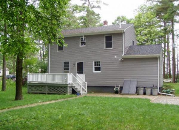 Gray two-story house with a white deck, surrounded by trees and green lawn.