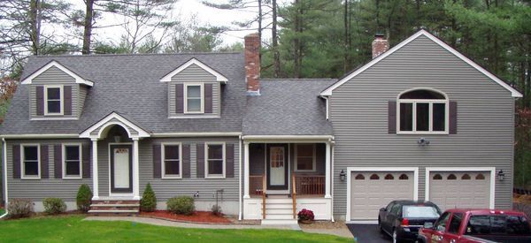 Gray house with multiple windows, shutters, and a two-car garage, cars parked in driveway.