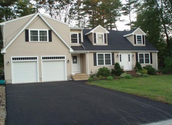 Beige house with black shutters and asphalt driveway. Two-car garage on the left. Front yard with small plants.