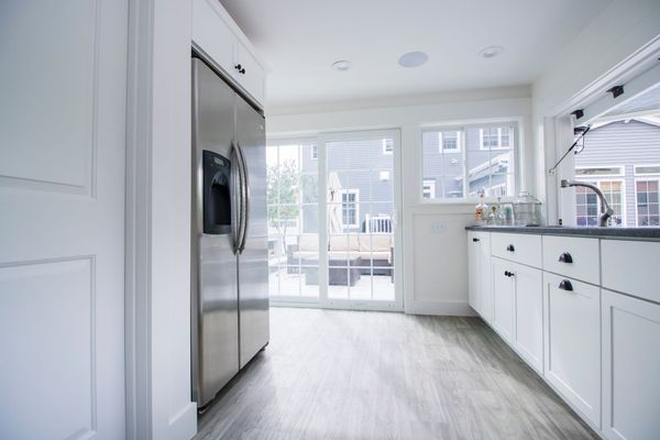 White kitchen with stainless steel fridge, cabinets, and sliding glass door to backyard.