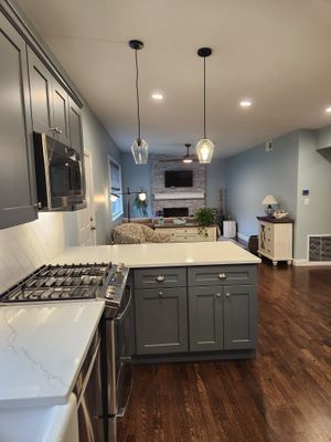 Gray kitchen with white countertops, leading into a living room with blue walls and a fireplace.