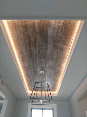 Wooden plank ceiling with perimeter lighting, a geometric chandelier, and light blue walls.