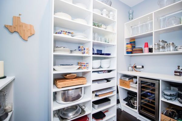 A white pantry with organized shelves holds dishes, glassware, and appliances, including a wine fridge.