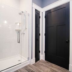 Bathroom with white tiled shower, black door, and gray wooden floor.