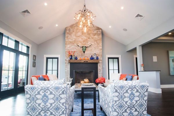 Living room with stone fireplace, patterned chairs, chandelier, and floor-to-ceiling windows.