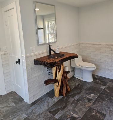 Bathroom with live-edge wooden vanity, black faucet, black sink, and white toilet. Tile floor, white walls.