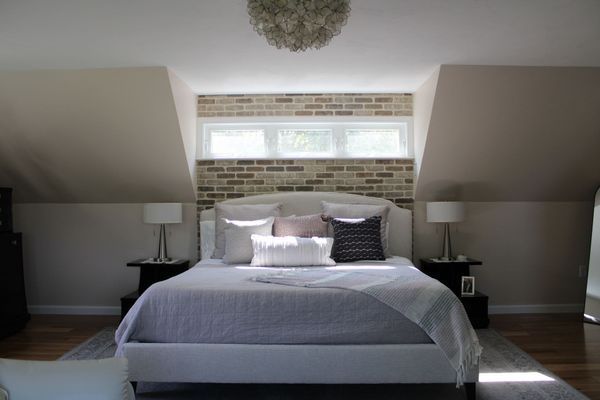 Bedroom with bed, brick wall, and sloped ceilings. Neutral tones, white bedding, and decorative pillows.