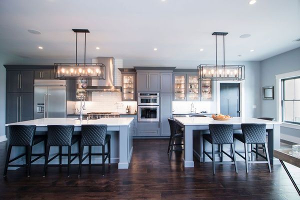 Modern kitchen with two islands, gray cabinets, dark wood floor, and black chairs.