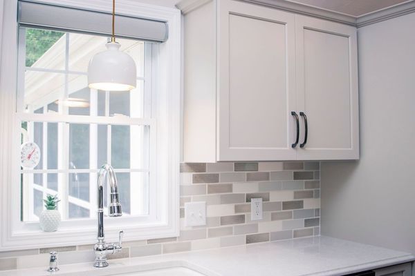 Kitchen with white cabinets, window, gray backsplash, and pendant light.