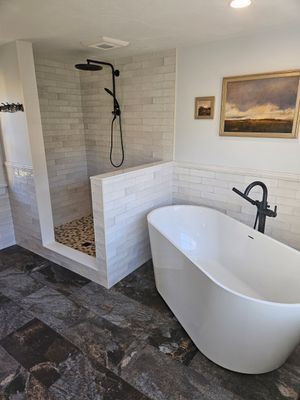 Modern bathroom with white freestanding tub, walk-in shower with pebble floor, and light tile walls.