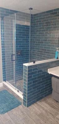 Bathroom with blue tile shower and gray wood-look tile floors.