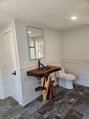 Bathroom with rustic wood vanity and black faucet. White toilet, stone floor and gray walls.