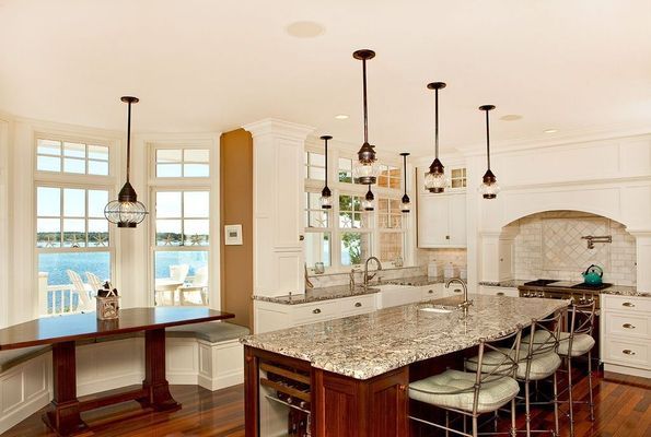 Kitchen with island, bar stools, pendant lights, windows, and a dark wood table overlooking water.