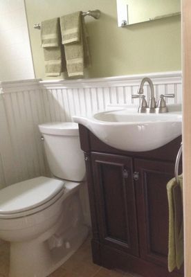 Bathroom with toilet, dark wood vanity with sink, and light green towels. Beadboard wall and olive green walls.