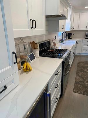 White kitchen with white cabinets, black hardware, quartz countertops, and stainless steel appliances.