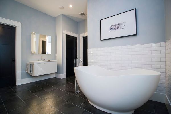 Modern bathroom with white soaking tub, black doors, blue walls, and black tile.