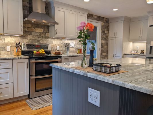 Modern kitchen with gray and white cabinets, island, stone backsplash, and flowers.