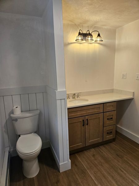 Bathroom with toilet and vanity. Light-colored wooden cabinets, and white walls with a dark floor.