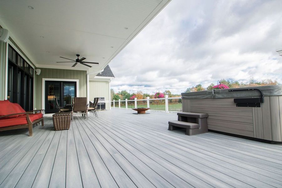 Gray composite deck with hot tub, outdoor furniture, and a view of water and trees under a cloudy sky.