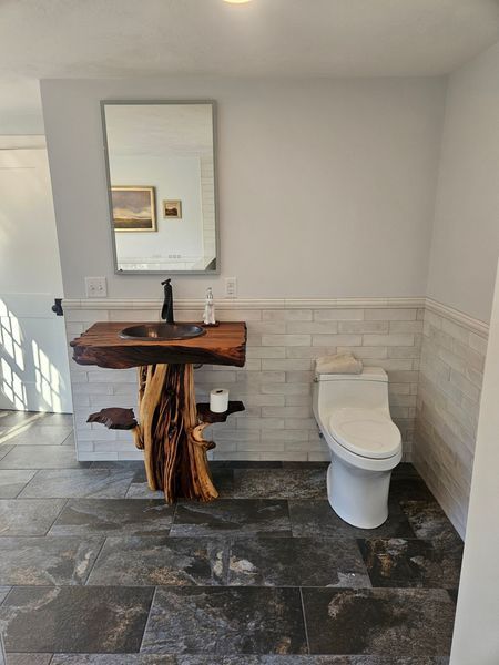Bathroom with live-edge wood vanity, black faucet, toilet, and large mirror on gray tile floor.