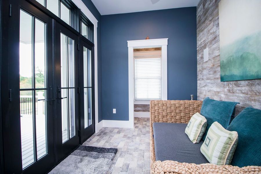 Dark blue room with wicker furniture, blue and green pillows, and glass doors leading to a deck.