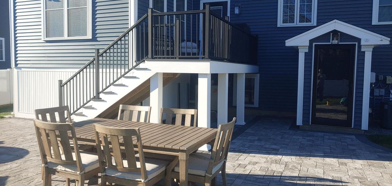 Outdoor patio with table and chairs. Stairs lead up to a deck. Blue building.
