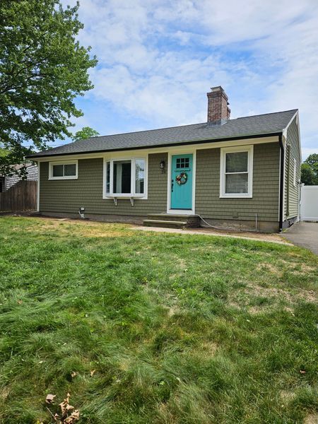 Green ranch-style house with a turquoise door, white trim, and a chimney under a blue sky.
