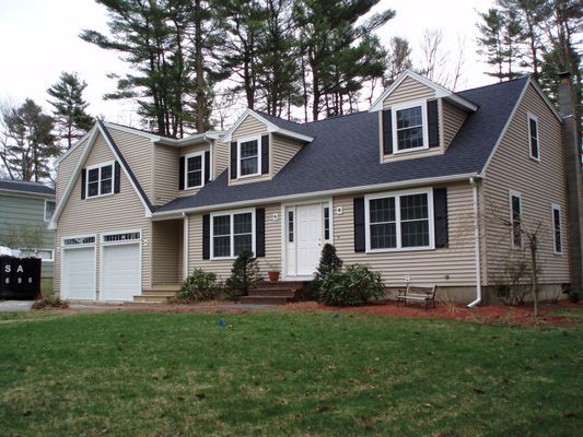 Beige house with black shutters and a dark blue roof. Two-car garage and dormers.