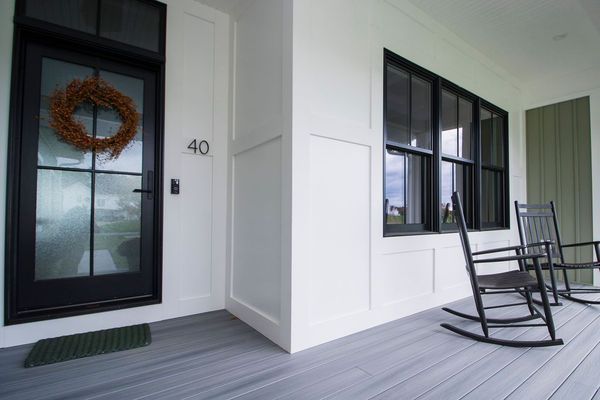 Black front door with wreath, number 40, and rocking chairs on a porch. White walls, gray floor.