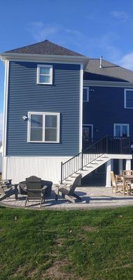 Back of a two-story blue house with a white base. Outdoor patio with seating and stairs. Blue sky.