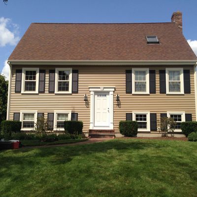 Beige house with brown roof, black shutters, white door, and green lawn.