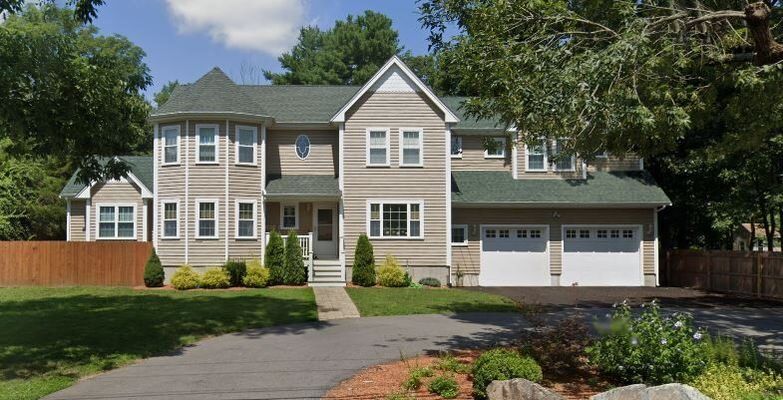Beige two-story house with green roof and attached two-car garage, set on a green lawn.