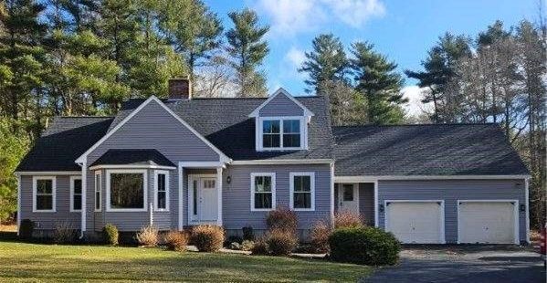 Gray house with a dark roof, two-car garage, and lush green lawn surrounded by trees on a sunny day.