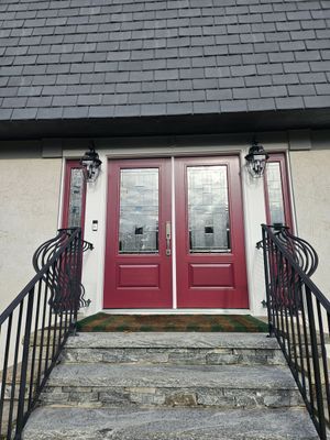 Red double doors with sidelights, above stone steps and a black metal railing.