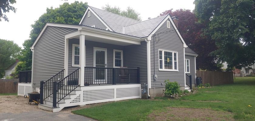Gray house with porch, black railings, and white trim, on a green lawn.