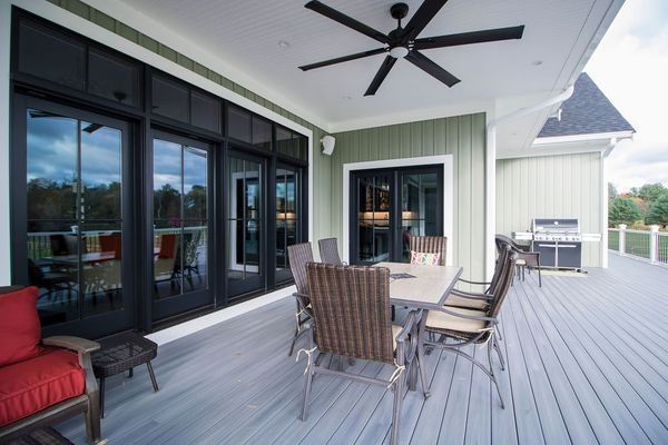 Outdoor patio with gray deck, dining set, red sofa, and black-framed glass doors.